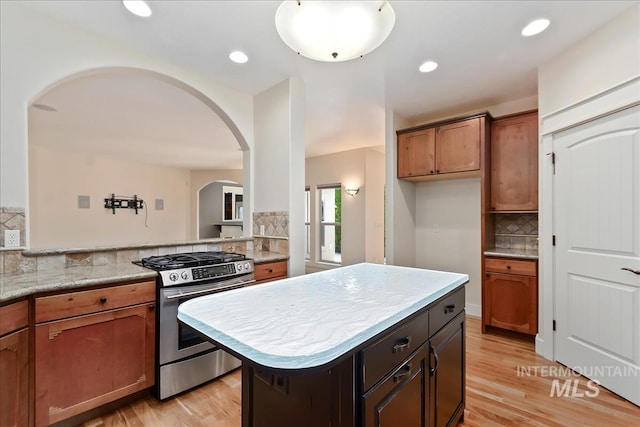 kitchen with stainless steel range with gas cooktop, recessed lighting, arched walkways, light wood-type flooring, and backsplash