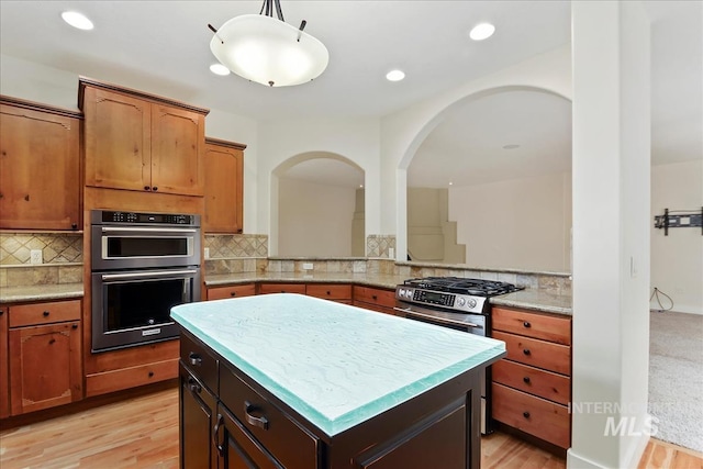 kitchen featuring tasteful backsplash, double oven, stainless steel range with gas cooktop, and a kitchen island