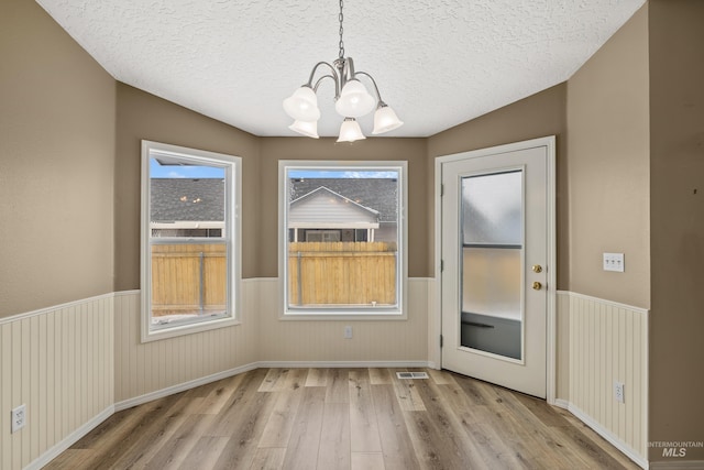 unfurnished dining area with a notable chandelier, a textured ceiling, and light hardwood / wood-style floors