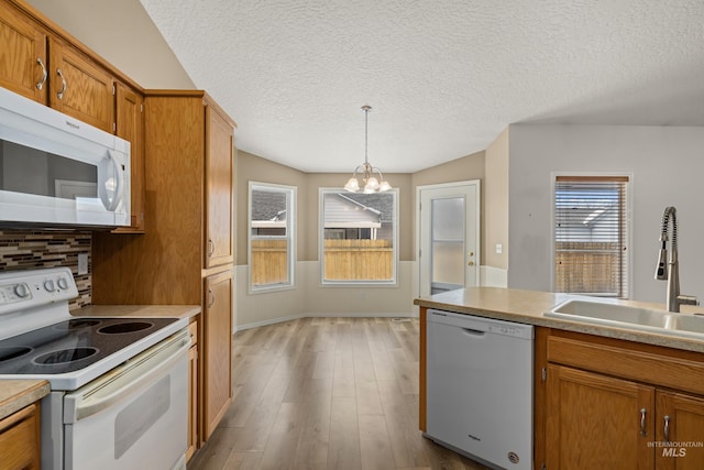 kitchen featuring pendant lighting, sink, white appliances, a notable chandelier, and light wood-type flooring