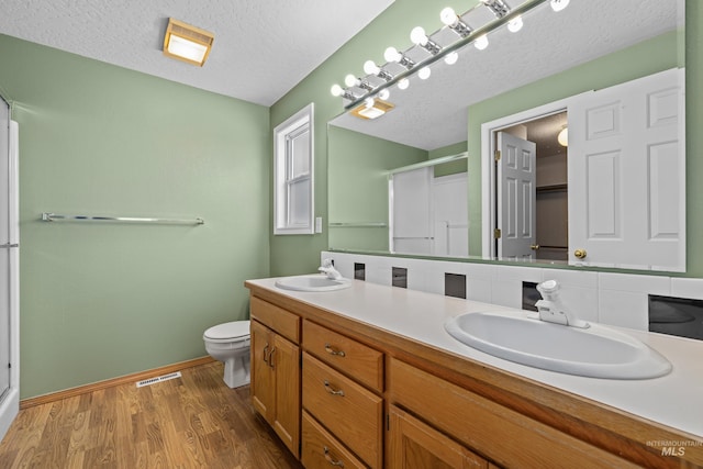 bathroom featuring hardwood / wood-style floors, vanity, an enclosed shower, toilet, and a textured ceiling