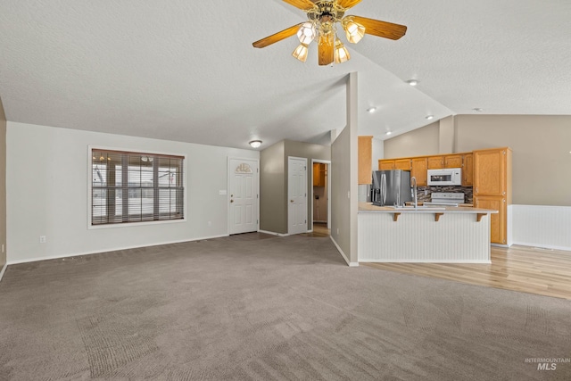 unfurnished living room with vaulted ceiling, light colored carpet, ceiling fan, and a textured ceiling