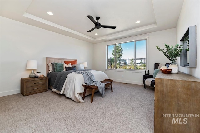 bedroom with ceiling fan, light colored carpet, and a tray ceiling