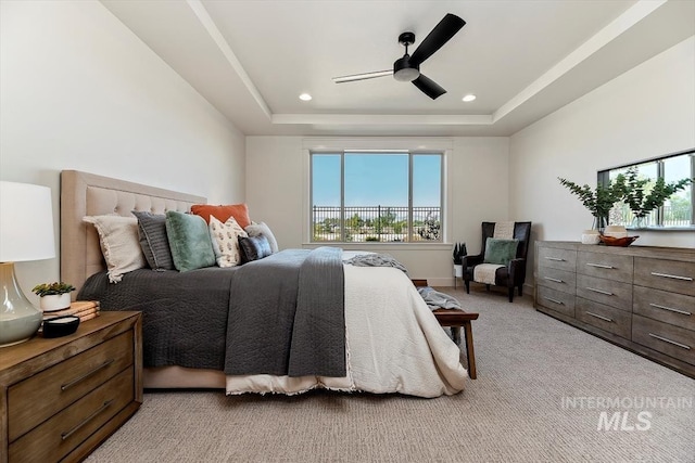 bedroom featuring ceiling fan, a tray ceiling, and light carpet