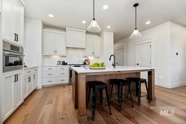 kitchen with an island with sink, appliances with stainless steel finishes, backsplash, pendant lighting, and white cabinets