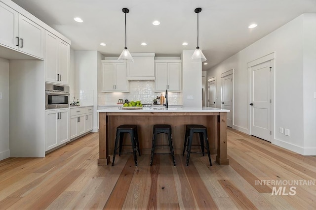 kitchen with decorative light fixtures, white cabinets, an island with sink, and light hardwood / wood-style floors