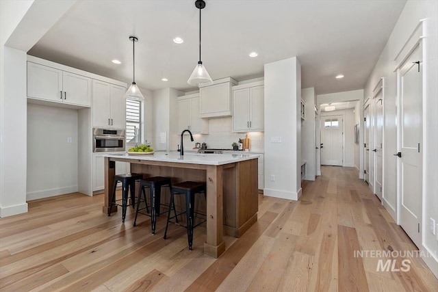 kitchen with decorative light fixtures, white cabinetry, a kitchen island with sink, and oven