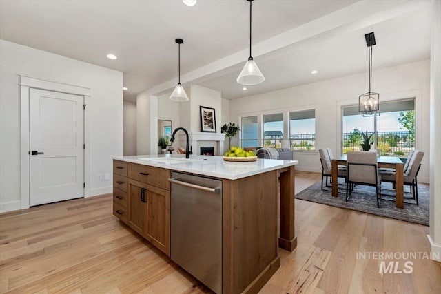 kitchen featuring decorative light fixtures, dishwasher, light hardwood / wood-style floors, sink, and a kitchen island with sink