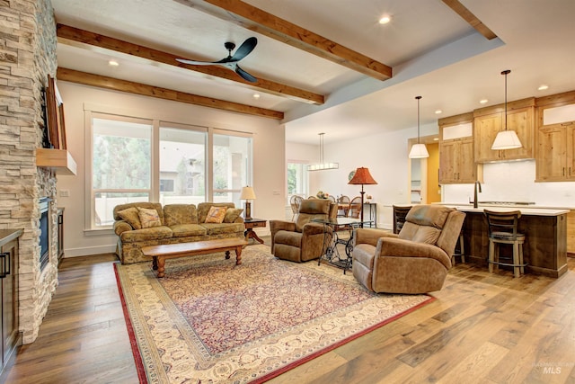 living room featuring beam ceiling, wood-type flooring, ceiling fan, and a fireplace