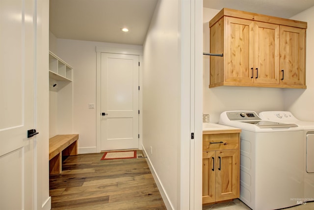 clothes washing area with cabinets, washing machine and clothes dryer, and wood-type flooring