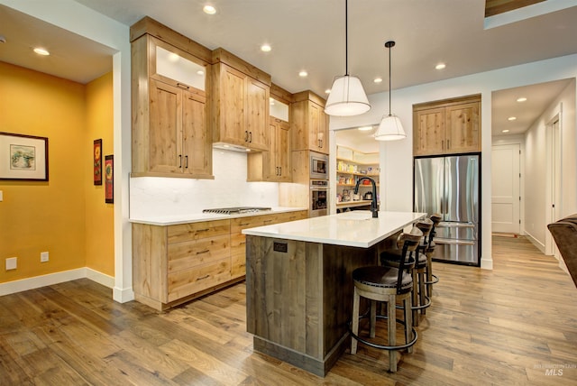 kitchen featuring decorative light fixtures, an island with sink, sink, backsplash, and stainless steel appliances