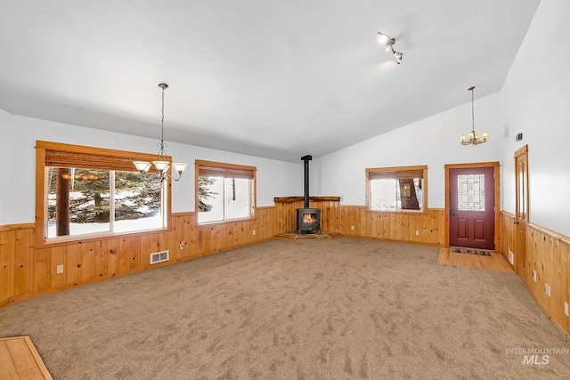 unfurnished living room with visible vents, a notable chandelier, a wood stove, and wainscoting