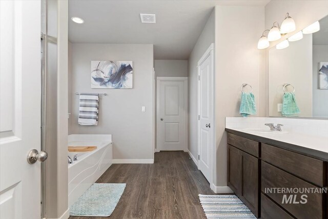 22924 Fargo Rd, Parma, ID 83660 - bathroom featuring vanity, a garden tub, wood finished floors, baseboards, and visible vents