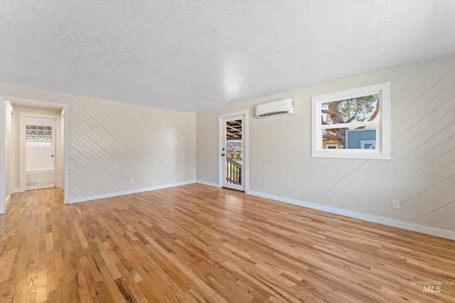 interior space with baseboards, a textured ceiling, a wall mounted air conditioner, and light wood-style floors