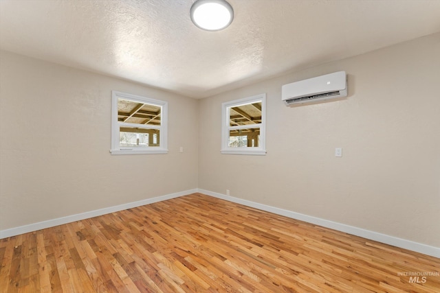 unfurnished room with light wood finished floors, a textured ceiling, a wall mounted AC, and baseboards