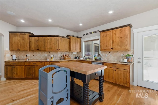 kitchen featuring light wood-style floors, brown cabinets, stainless steel dishwasher, and tasteful backsplash