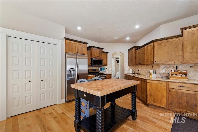 kitchen featuring light wood-style flooring, appliances with stainless steel finishes, arched walkways, and backsplash