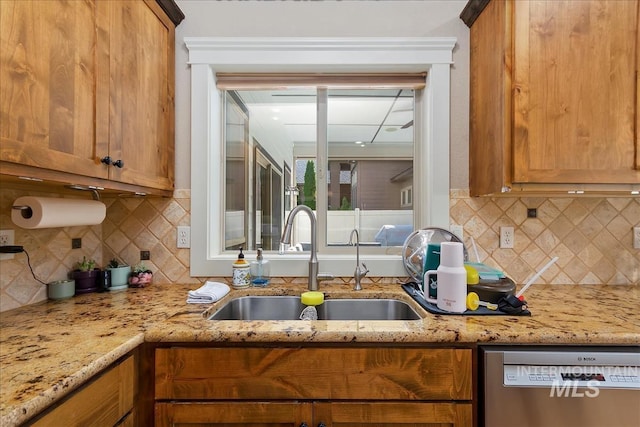 kitchen featuring stainless steel dishwasher, brown cabinetry, a sink, and light stone counters