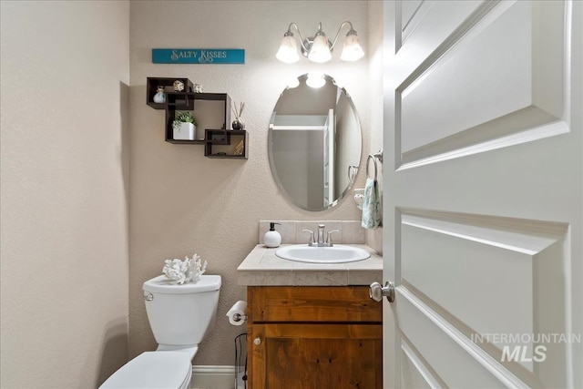 half bathroom featuring a textured wall, vanity, and toilet