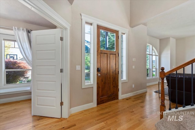 foyer entrance with light wood-type flooring, baseboards, and stairway