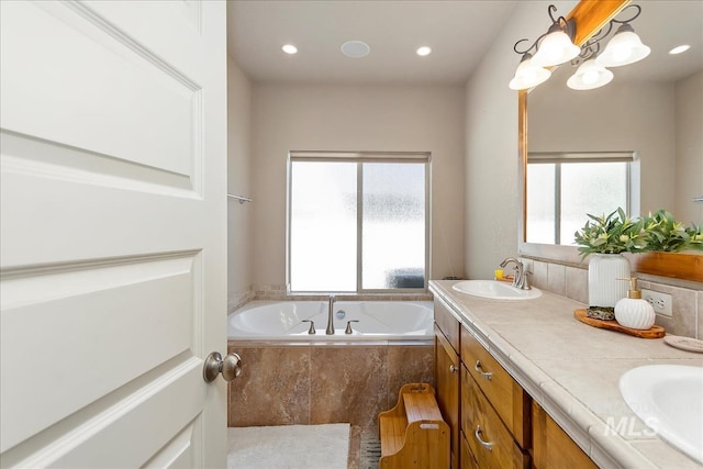 bathroom with double vanity, a sink, a bath, and recessed lighting