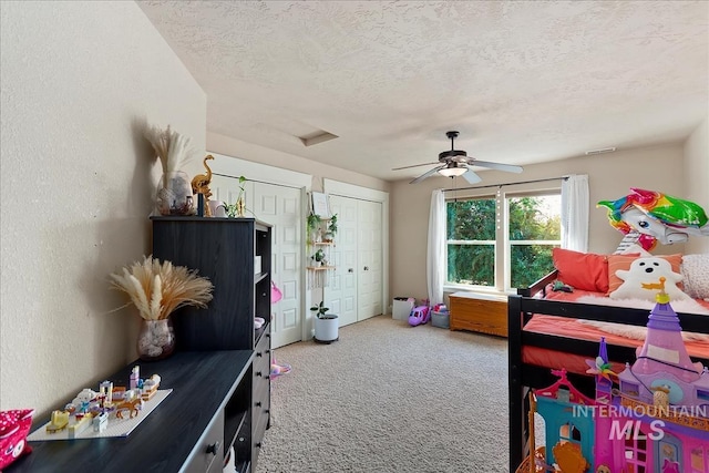 bedroom featuring carpet, multiple closets, a textured wall, a ceiling fan, and a textured ceiling