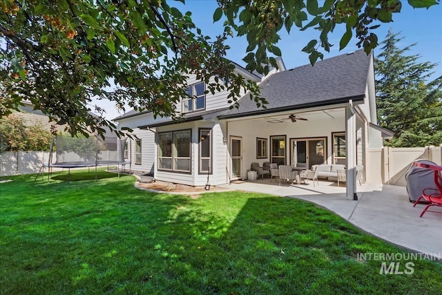 rear view of house with a ceiling fan, a lawn, a patio, a trampoline, and fence