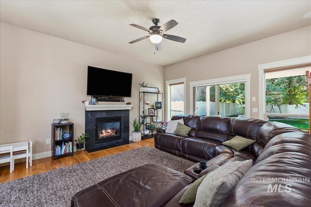 living room with ceiling fan, a fireplace, baseboards, and wood finished floors