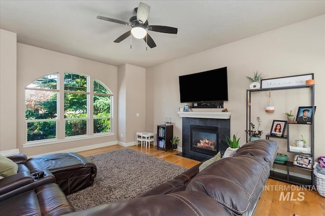 living room featuring ceiling fan, a tiled fireplace, wood finished floors, and baseboards