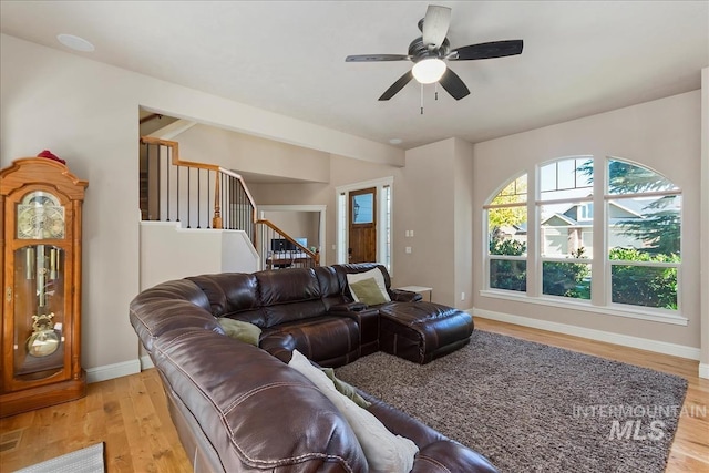 living area with light wood-type flooring, baseboards, stairway, and ceiling fan