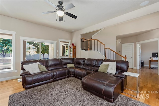 living area featuring stairs, light wood-type flooring, a ceiling fan, and baseboards