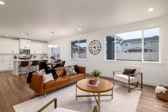 living room featuring baseboards, recessed lighting, light wood-style flooring, and an inviting chandelier