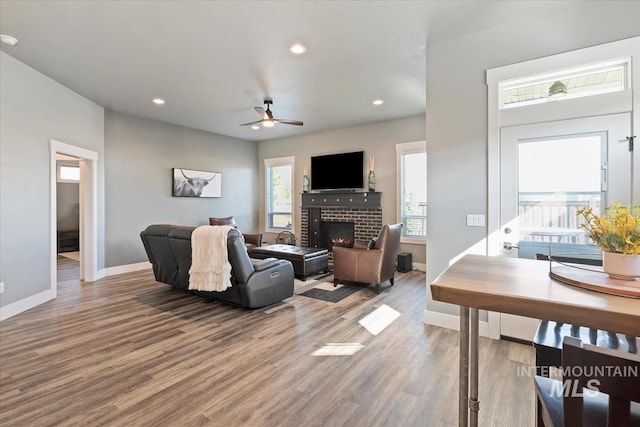 living area with baseboards, a ceiling fan, a brick fireplace, and wood finished floors