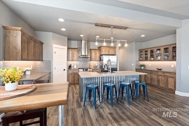 kitchen with wall chimney range hood, stainless steel appliances, dark wood finished floors, and tasteful backsplash