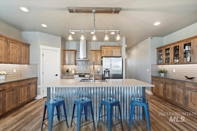 kitchen featuring decorative backsplash, dark wood-style floors, wall chimney range hood, a kitchen bar, and stainless steel appliances