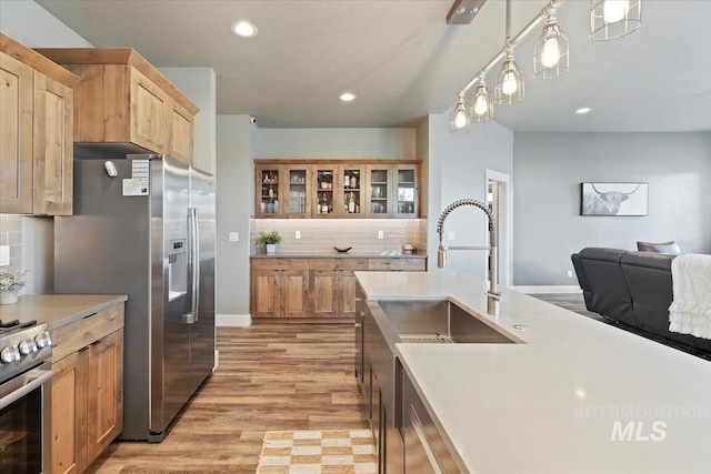 kitchen with light countertops, stainless steel appliances, light wood-type flooring, backsplash, and glass insert cabinets