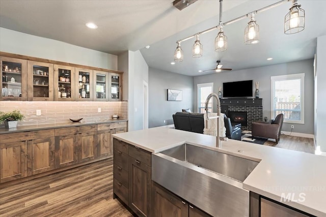 kitchen featuring a sink, a lit fireplace, a ceiling fan, and wood finished floors