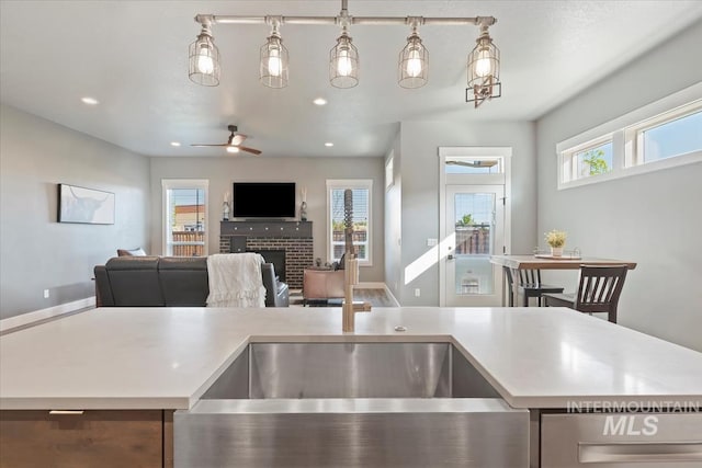 kitchen featuring a brick fireplace, open floor plan, ceiling fan, recessed lighting, and light countertops