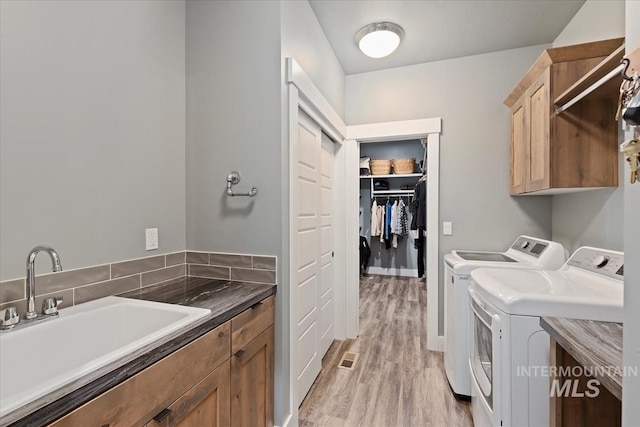 washroom with a sink, washing machine and dryer, light wood finished floors, and cabinet space