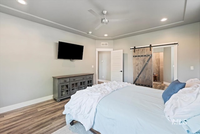 bedroom with visible vents, wood finished floors, a barn door, baseboards, and recessed lighting