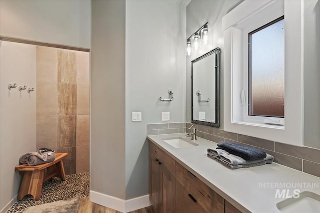 bathroom with vanity, baseboards, backsplash, and walk in shower
