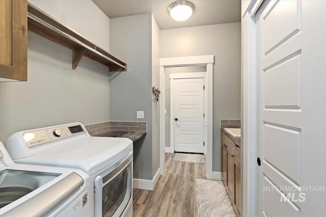 clothes washing area featuring separate washer and dryer, baseboards, light wood-type flooring, and cabinet space