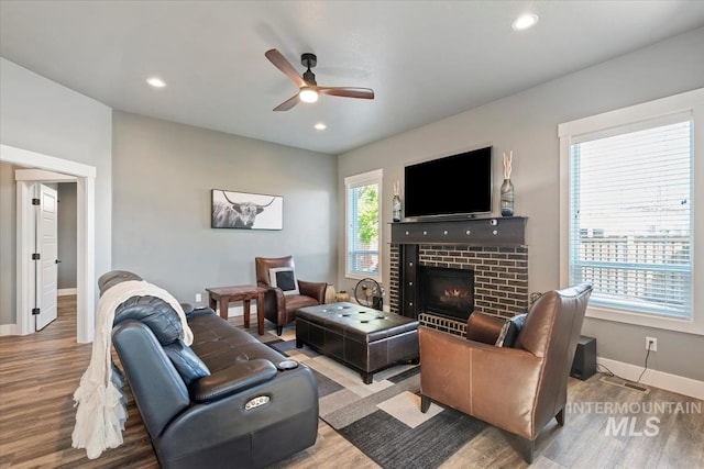 living room with a brick fireplace, a ceiling fan, baseboards, recessed lighting, and wood finished floors