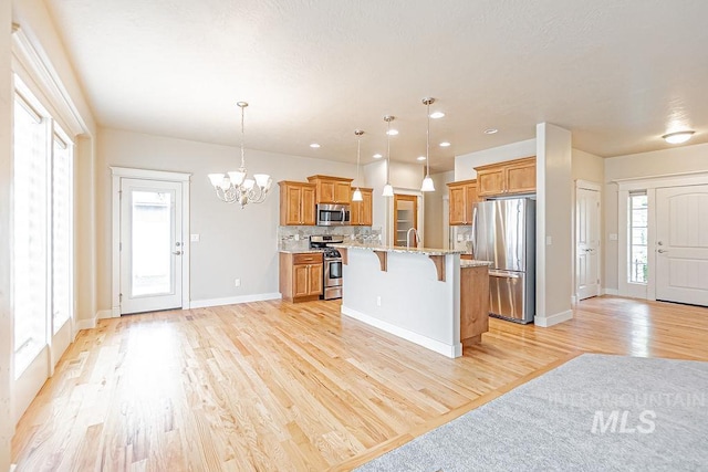 7053 W Butte Ln, Boise, ID 83704 - kitchen with stainless steel appliances, a breakfast bar area, light wood-type flooring, a chandelier, and brown cabinets