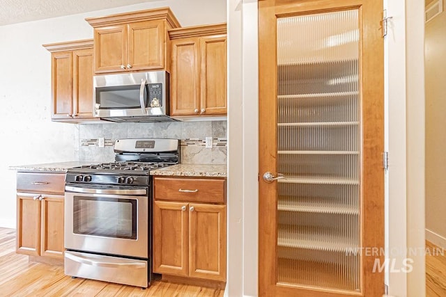 7053 W Butte Ln, Boise, ID 83704 - kitchen featuring appliances with stainless steel finishes, light wood-type flooring, decorative backsplash, and light stone countertops
