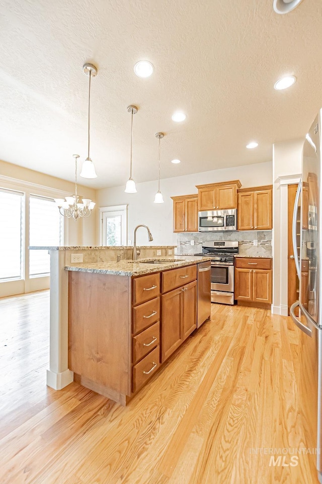 7053 W Butte Ln, Boise, ID 83704 - kitchen featuring appliances with stainless steel finishes, a textured ceiling, a sink, light wood-style floors, and a kitchen island with sink