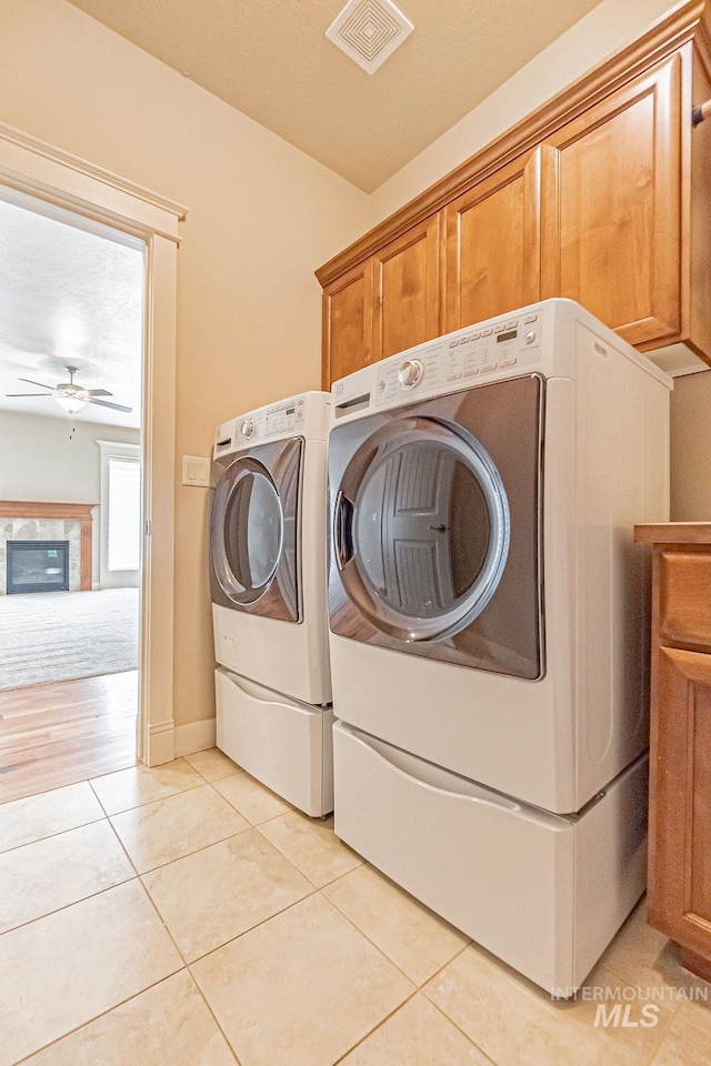 7053 W Butte Ln, Boise, ID 83704 - laundry area featuring washer and clothes dryer, cabinet space, ceiling fan, light tile patterned floors, and a glass covered fireplace