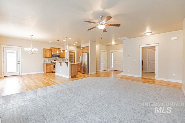 7053 W Butte Ln, Boise, ID 83704 - unfurnished living room with light wood-style floors, a ceiling fan, baseboards, a chandelier, and a sink