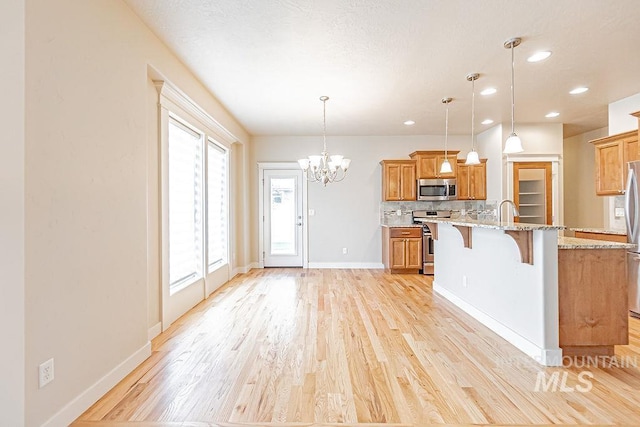 7053 W Butte Ln, Boise, ID 83704 - kitchen featuring stainless steel appliances, a kitchen bar, light wood finished floors, backsplash, and a chandelier