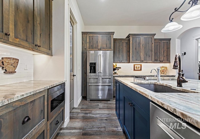 kitchen featuring pendant lighting, sink, stainless steel appliances, light stone countertops, and dark brown cabinets